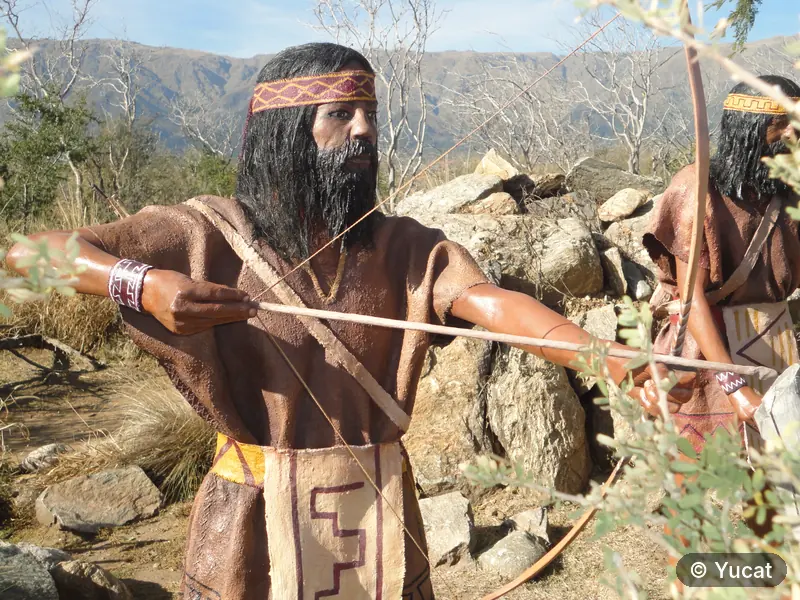 Dos esculturas de arqueros comechingones con las Sierras de los Comechingones de fondo.